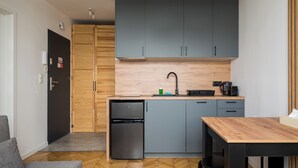 A compact kitchen with grey cabinets, a small refrigerator, and a wooden countertop. - Puławska Urban Nest Apartment (Warszawa)