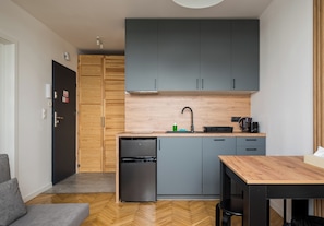 A compact kitchen with grey cabinets, a small refrigerator, and a wooden countertop. - Puławska Urban Nest Apartment (Warszawa)