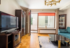 Un salon comprenant un téléviseur, un canapé, une table basse en verre et une vue dégagée sur l’extérieur grâce à une grande fenêtre.