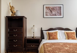 Une chambre à coucher avec une commode en bois, une table de chevet avec une lampe et un lit recouvert d’une literie à motifs floraux.