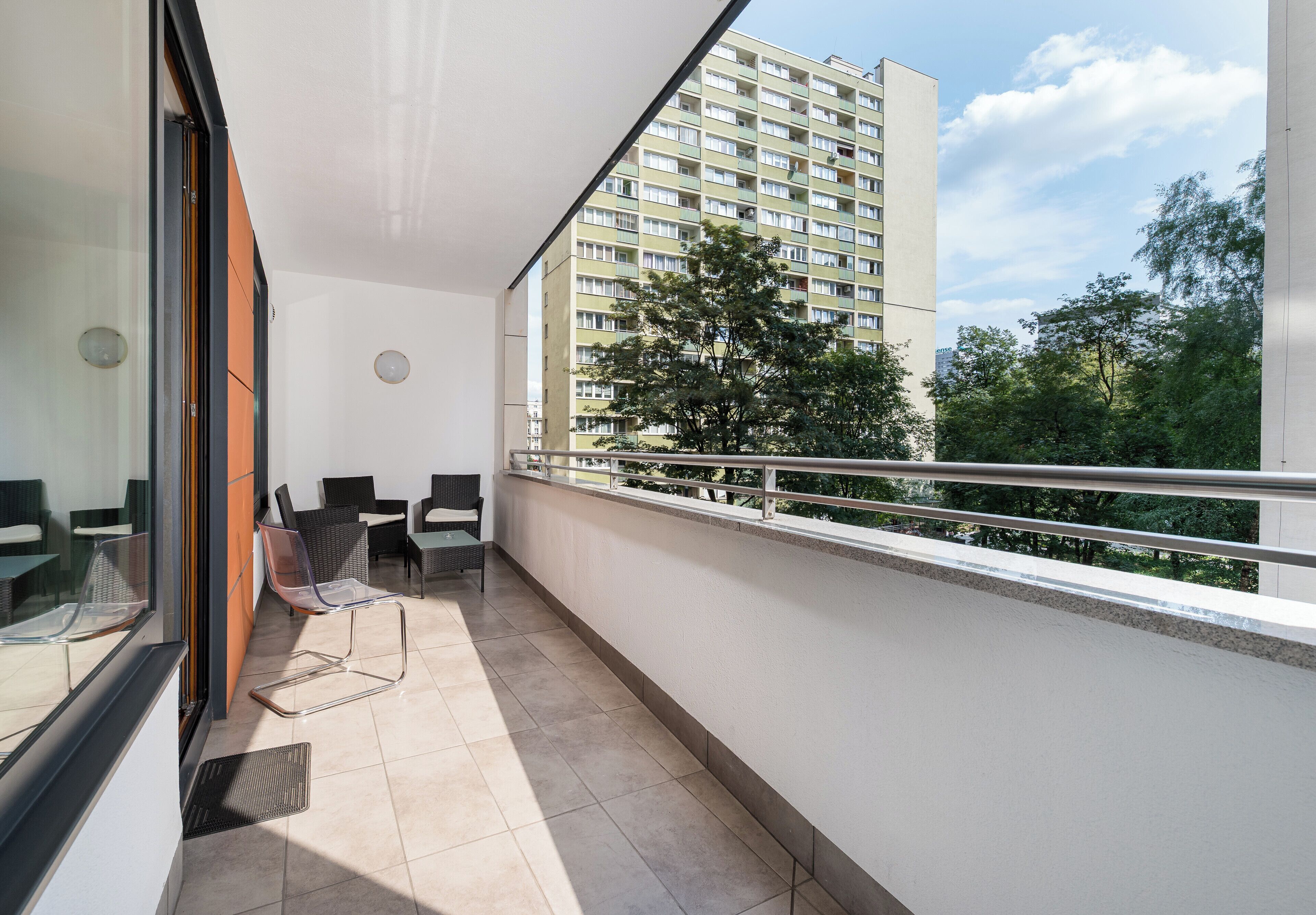 A balcony with a view of a high-rise building, outdoor furniture, and a tree.