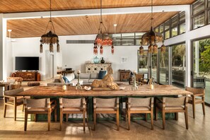 A spacious living area with a large wooden dining table, multiple chairs, and hanging pendant lights.
