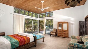 A bedroom with a large bed, a chair, a wooden dresser, and a ceiling fan.
