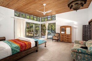 A bedroom with a large bed, a chair, a wooden dresser, and a ceiling fan.