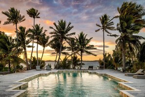 A poolside area with lounge chairs and a view of the sea at sunset.