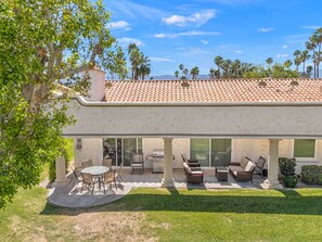Une terrasse couverte, aménagée avec du mobilier d’extérieur, un barbecue et offrant une vue sur les palmiers et les montagnes.