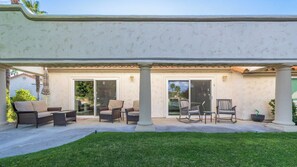 An outdoor patio with a seating area, a potted plant, and a building with a textured facade. - 3 Bedroom Desert Retreat Steps From the Pool (Palm Desert)