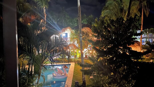 A nighttime view of a resort with a swimming pool, palm trees, and a building with illuminated windows.