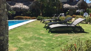 A poolside area with lounge chairs, a thatched-roof building, and a clear blue pool.