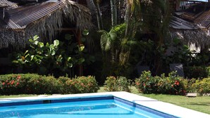 A swimming pool with a clear blue water surface, surrounded by lush greenery and flowering plants.