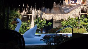 A swan-shaped water feature in a tropical setting with a thatched-roof structure in the background.