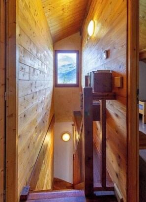 A wooden interior with a staircase leading to a window with a view.