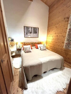 A bedroom with a wooden headboard, a bed with white bedding, a nightstand with a lamp, and a wall-mounted picture.