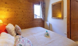 A bedroom with a wooden ceiling, a window with curtains, a bed with pillows, and a bedside table.