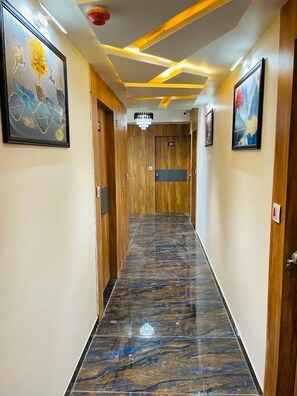 Un pasillo de hotel con puertas de madera, suelo de mármol y obras de arte en las paredes.