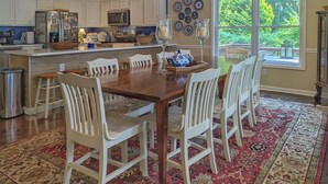 A dining area with a wooden table, white chairs, a chandelier, and a large window with a view of trees. - The Haven Adjoining houses for large groups/families Lake Junaluska (Lake Junaluska)
