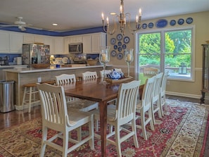 A dining area with a wooden table, white chairs, a chandelier, and a large window with a view of trees. - The Haven Adjoining houses for large groups/families Lake Junaluska (Lake Junaluska)