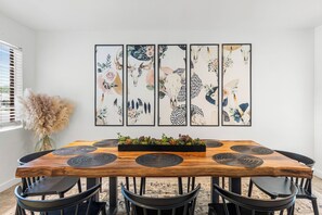 Ein Essbereich mit einem Holztisch, sechs Stühlen und einer Wand mit fünf gerahmten Kunstwerken.