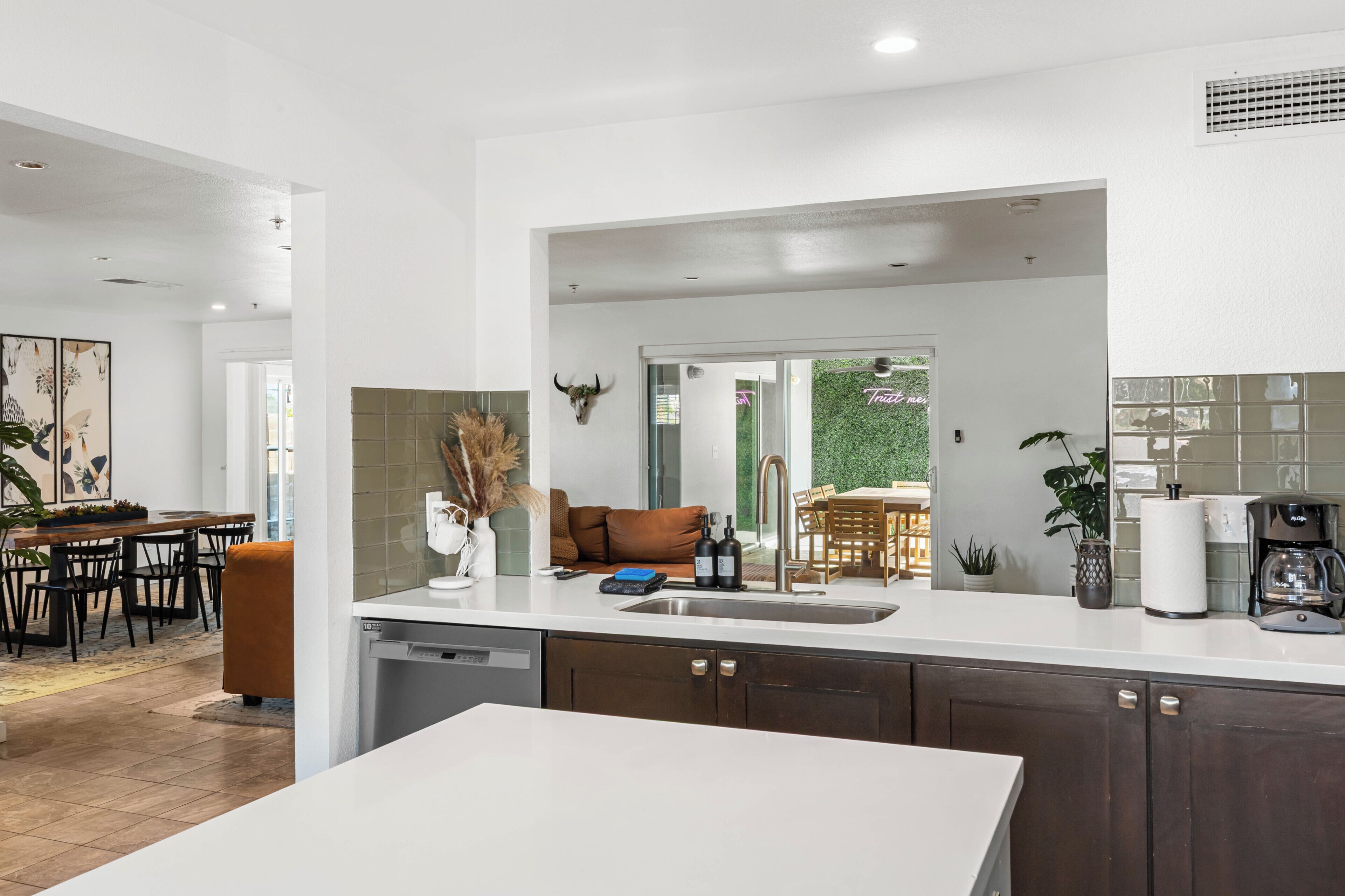 A modern kitchen with a central island, a dining area with a wooden table and chairs, and a living space with a sofa and decorative wall art.