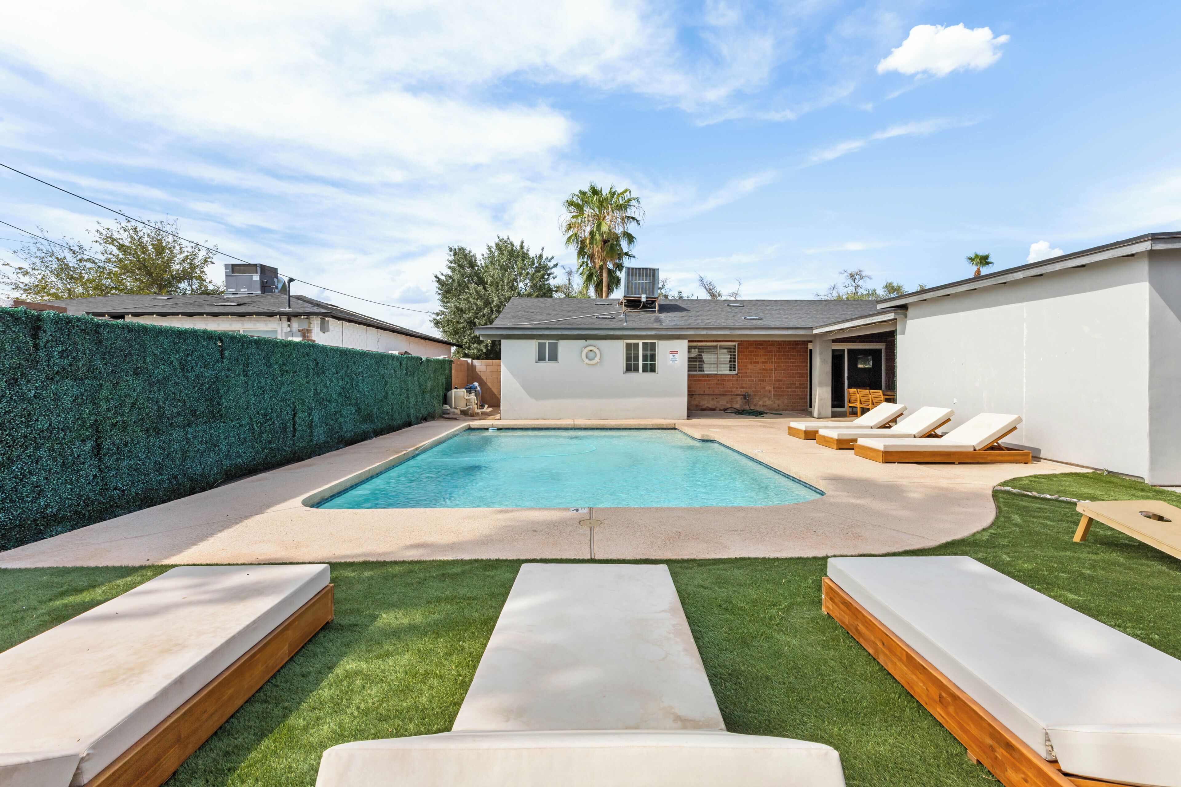 A backyard with a swimming pool, lounge chairs, and a well-maintained lawn.