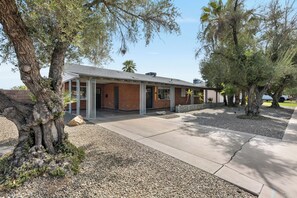 A two-story building with a brick facade, a covered patio area, and a gravel driveway. - Scottsdale Old Town Palm Oasis 🌵⛳ Heated Pool, Ping Pong Near Old Town (Scottsdale)