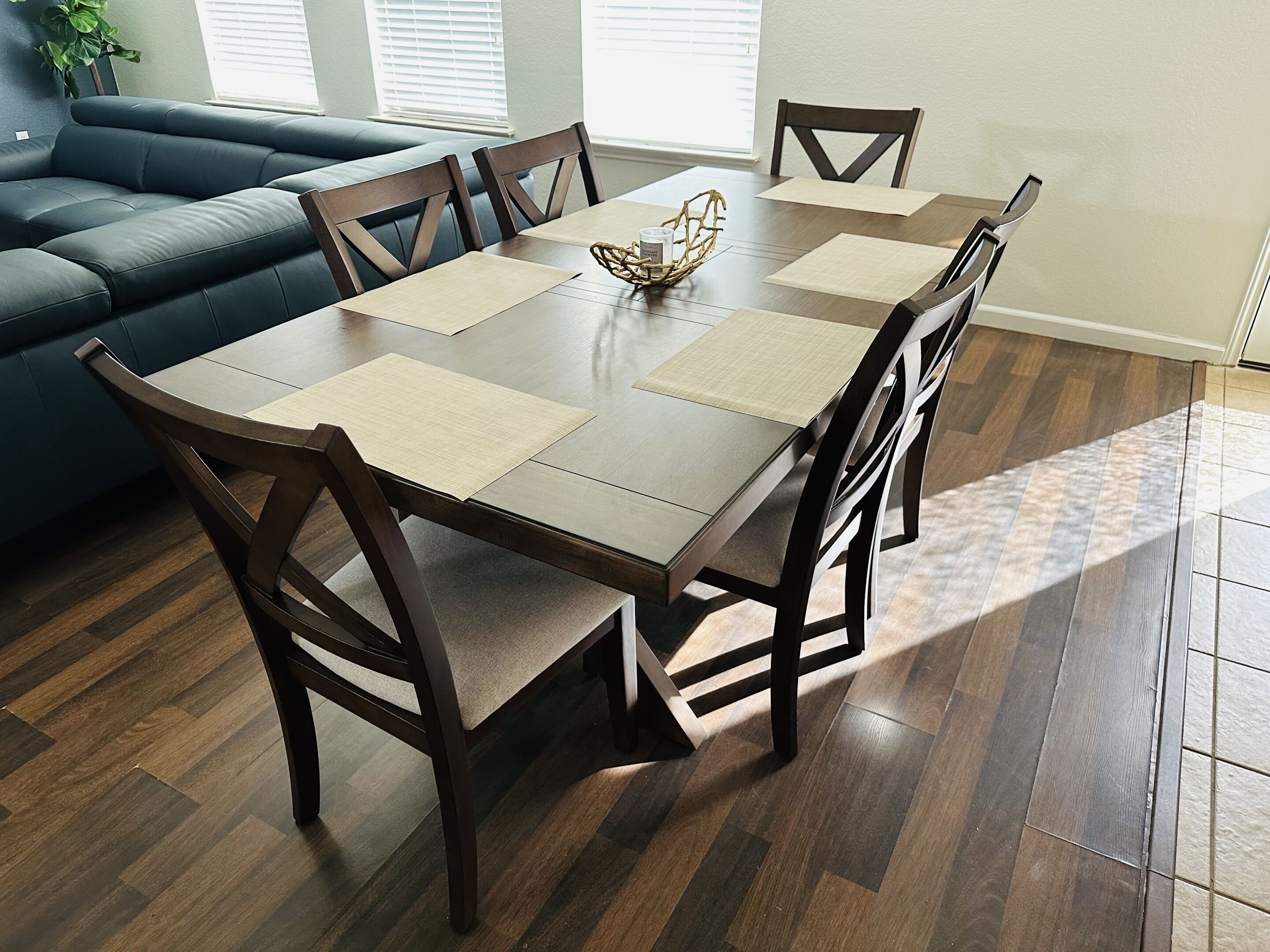 Un comedor con una mesa rectangular, seis sillas y una cesta tejida sobre la mesa.