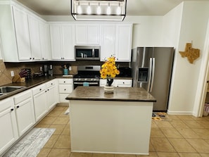 A kitchen with white cabinets, stainless steel appliances, a central island with a vase of flowers, and a Texas-shaped wall decoration.
