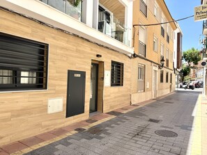 A building with a wooden facade, a closed black door labeled 'CONT. AGUA,' and a visible fire alarm. - SR Playa de los Boliches 2-Bedroom Apartment, Downtown Fuengirola (Fuengirola)