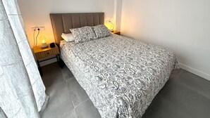 Et soveværelse med en seng, sengeborde, lamper og et gardin.