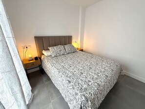 A bedroom with a bed, bedside lamps, a nightstand, and a curtain. - SR Playa de los Boliches 2-Bedroom Apartment, Downtown Fuengirola (Fuengirola)