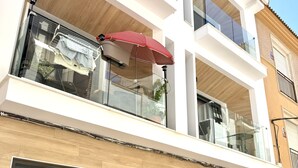 En moderne bygning med en balkon, en rød parasol og en dør med teksten 'CONTAGUA'.