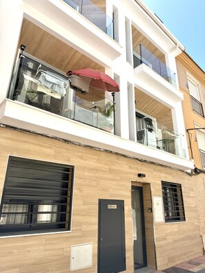 A modern building with a balcony, a red umbrella, and a door labeled 'CONTAGUA'. - SR Playa de los Boliches 2-Bedroom Apartment, Downtown Fuengirola (Fuengirola)