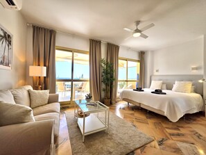 A hotel room with a bed, a sofa, a coffee table, a ceiling fan, and a view of the outdoors. - SR Romana Playa 545 Studio with a Wonderful Ocean View (Marbella)