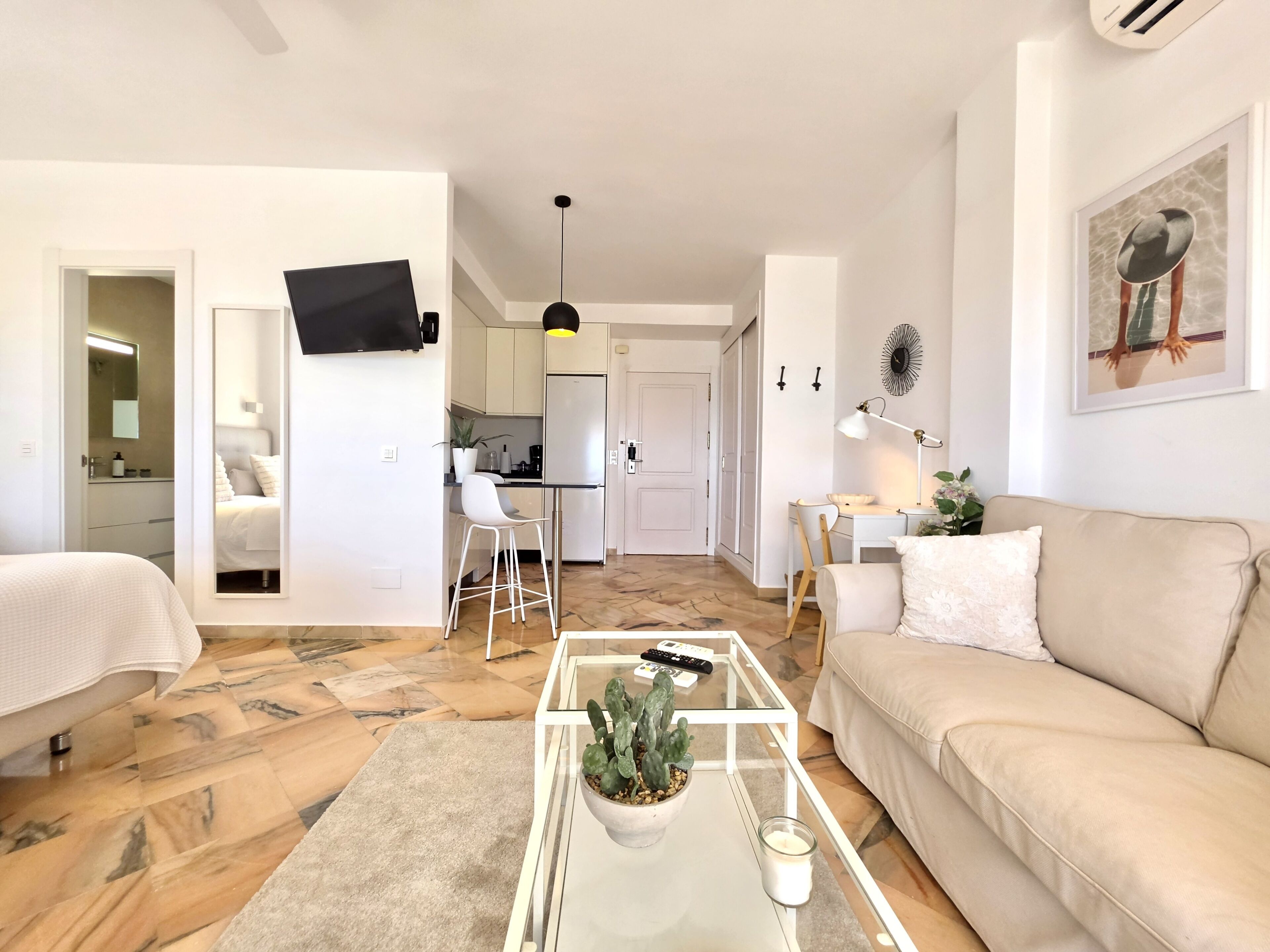 Uma sala de estar moderna com um sofá, uma mesa de centro com uma planta e uma TV fixada na parede.