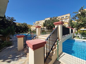 A pool area with a staircase leading to a building, surrounded by trees and a clear sky. - SR Romana Playa 545 Studio with a Wonderful Ocean View (Marbella)