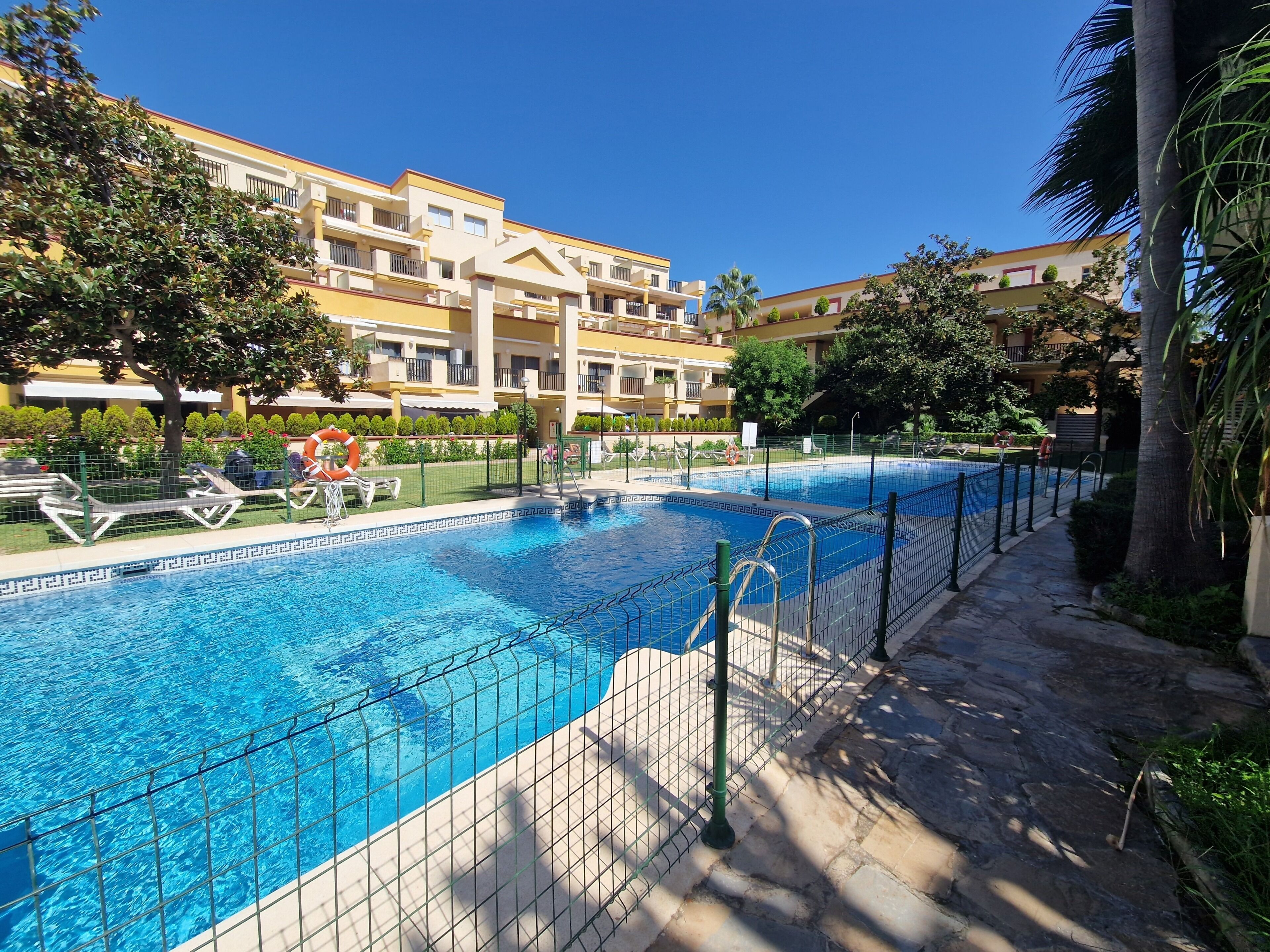 Une piscine à l’eau d’un bleu limpide, entourée d’une terrasse en pierre et d’une clôture en métal.