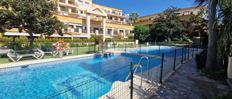 Une piscine à l’eau d’un bleu limpide, entourée d’une terrasse en pierre et d’une clôture en métal.