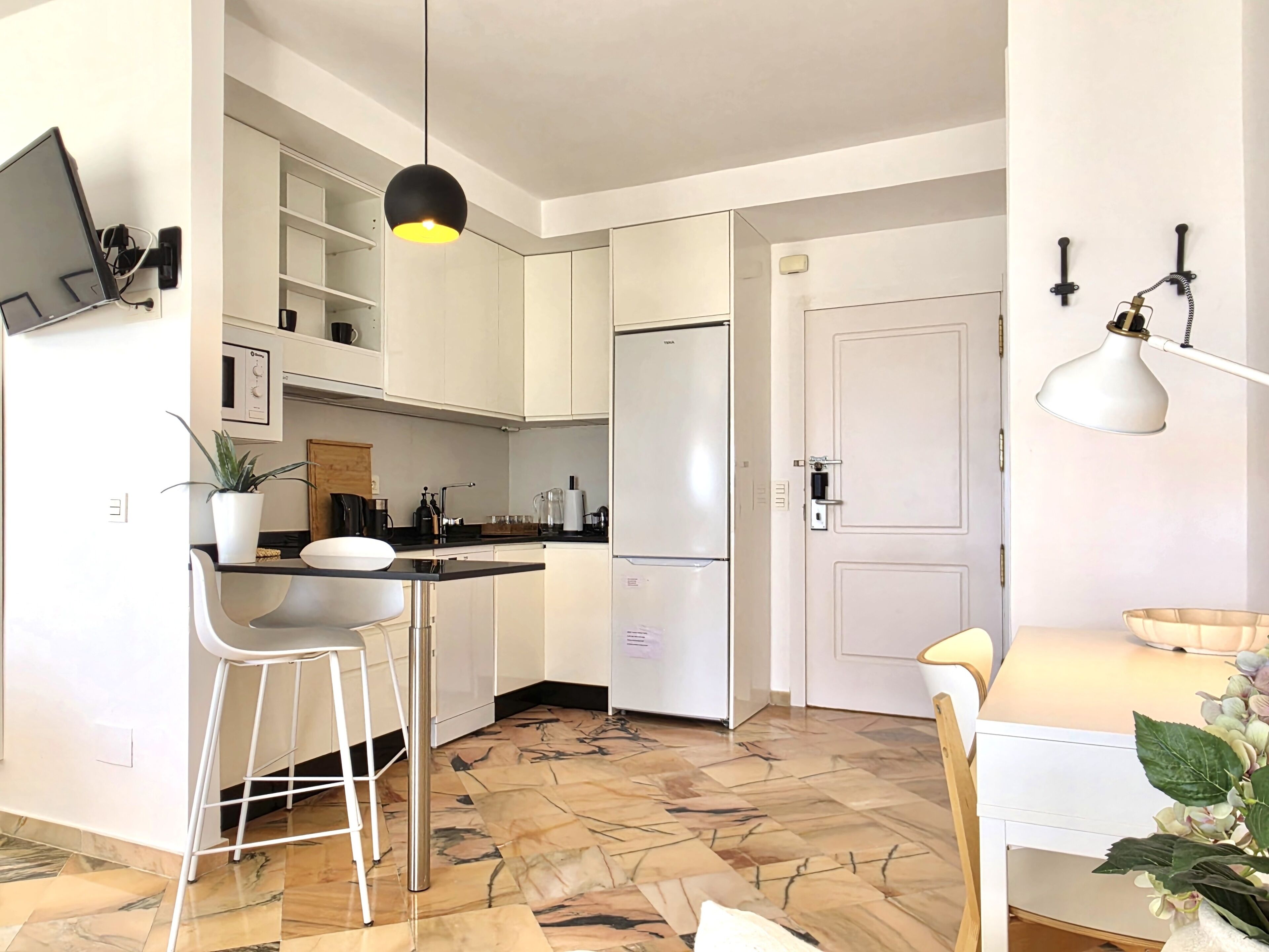 Een moderne keuken met witte kasten, een roestvrijstalen koelkast, een bar met krukken en een hanglamp.