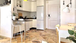 Een moderne keuken met witte kasten, een roestvrijstalen koelkast, een bar met krukken en een hanglamp.