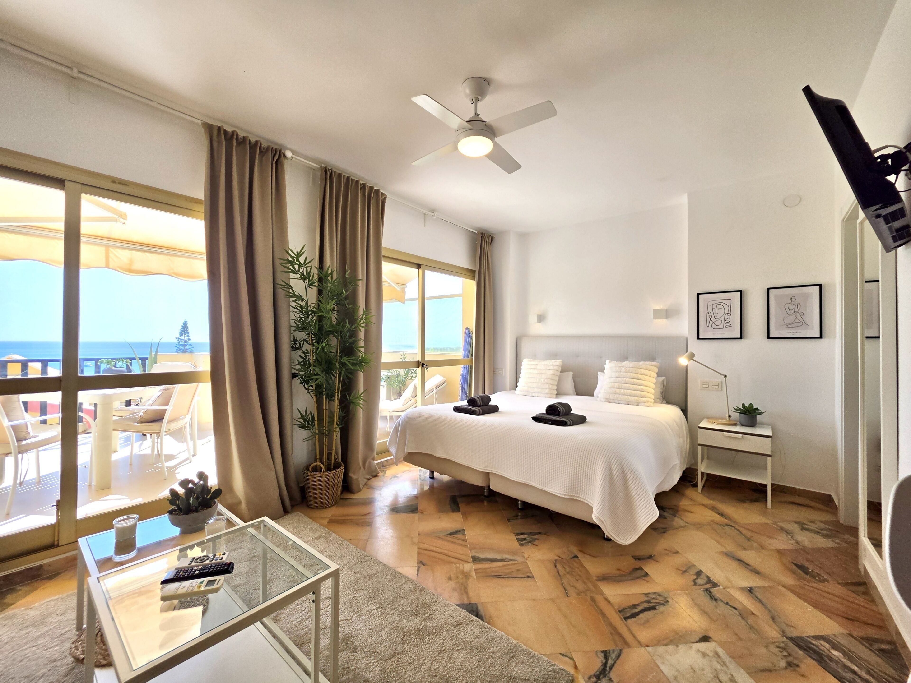 Une chambre d’hôtel avec un lit, un bureau, une chaise, une plante en pot et une vue sur la mer.