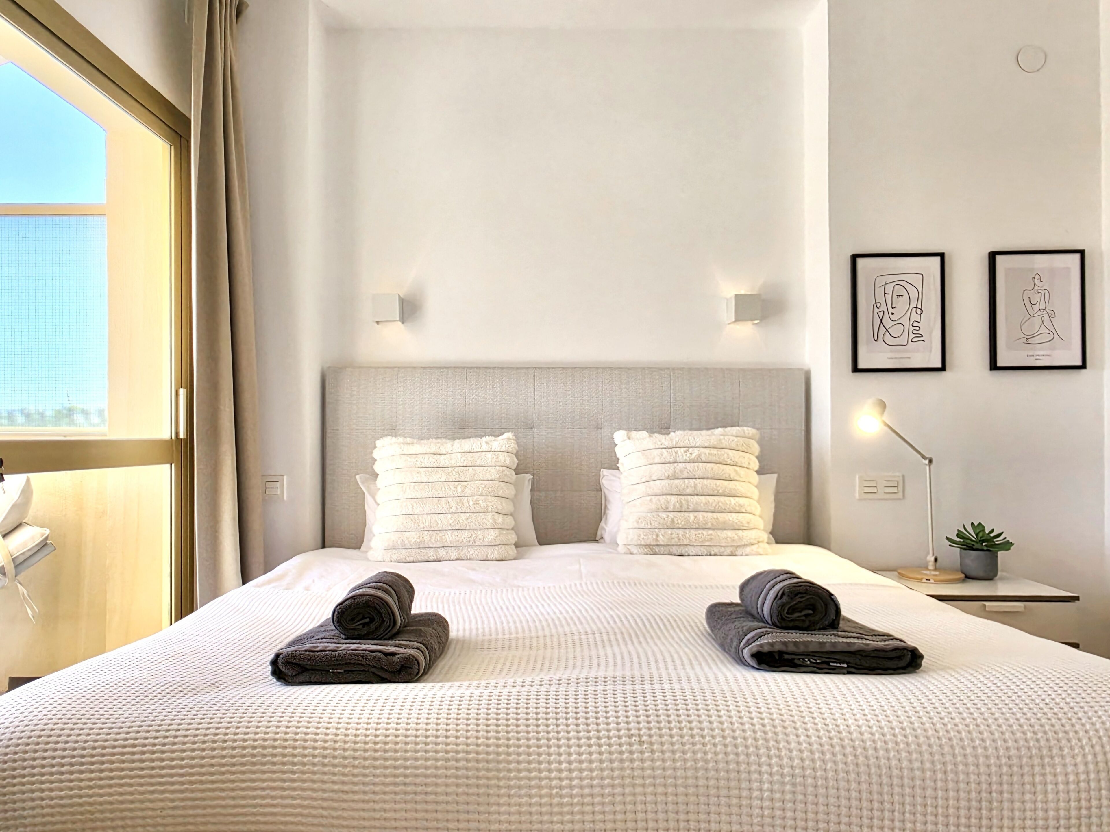 Une chambre d’hôtel avec un grand lit, deux oreillers, une lampe de chevet et des œuvres d’art accrochées au mur.