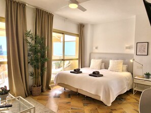 Habitación de hotel con cama, escritorio, una silla, una planta y vista al mar.