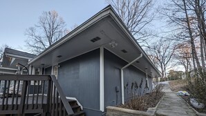 Un immeuble résidentiel à l’extérieur gris, avec un escalier en bois menant à une terrasse et un mur de soutènement en pierre.