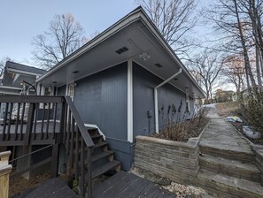 A residential building with a grey exterior, a wooden staircase leading to a deck, and a stone retaining wall. - Colony Home for Family Groups - Patio, Workspace (Marietta)