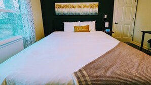 Une chambre d’hôtel avec un lit, un tableau au-dessus du lit, une fenêtre avec des rideaux et une porte.