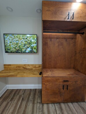 A room with a wooden cabinet, a mounted television displaying a nature scene, and a wooden floor. - Colony Home for Family Groups - Patio, Workspace (Marietta)