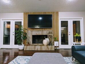 A living room with a fireplace, a flat-screen TV mounted above it, and a sofa. - Colony Home for Family Groups - Patio, Workspace (Marietta)