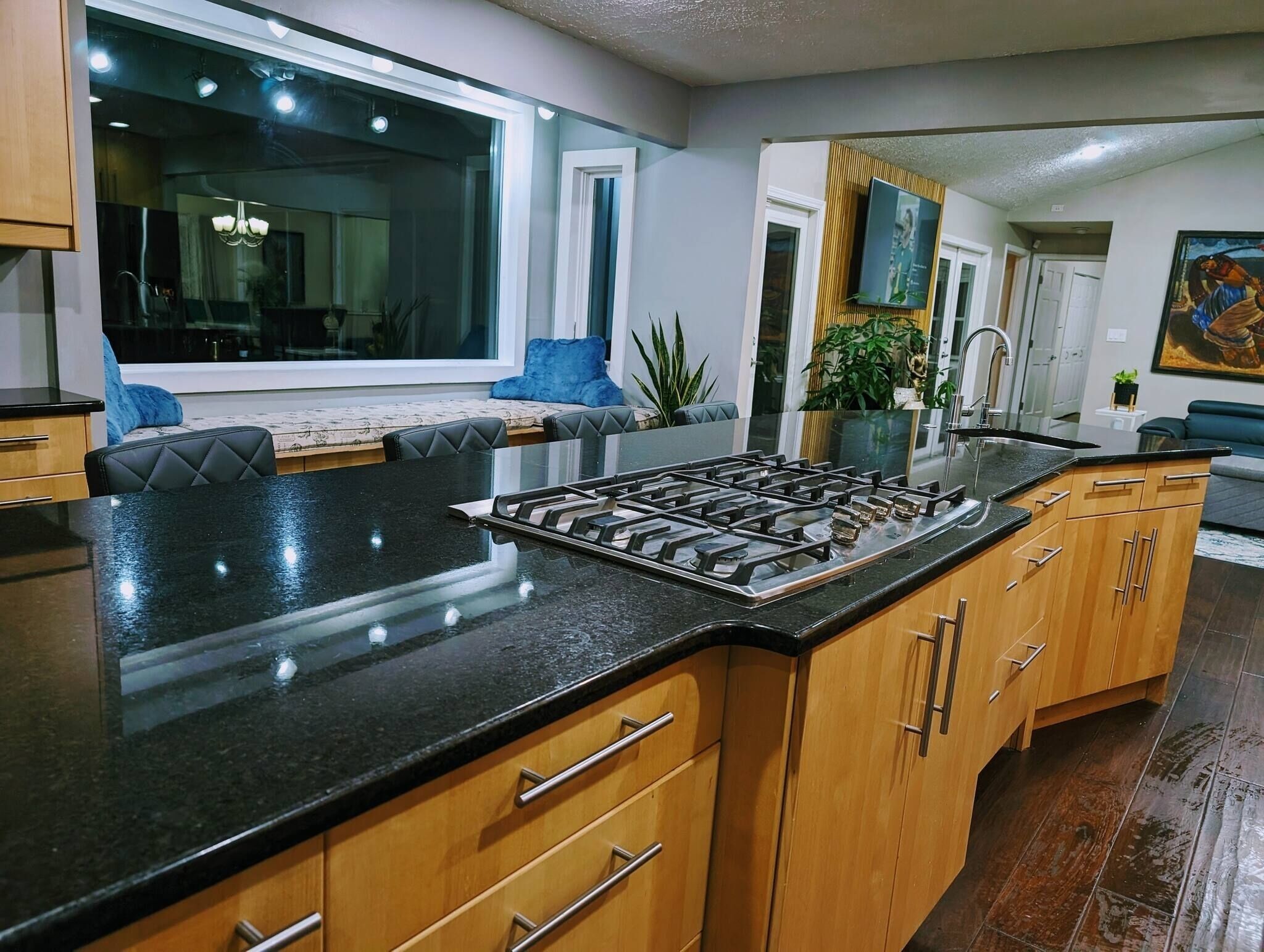 A modern kitchen with a central island, wooden cabinets, and a large window.
