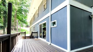 Une terrasse en bois avec une rambarde, un bâtiment à l’extérieur bleu et une porte donnant sur un espace abrité.