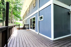 A wooden deck with a railing, a building with a blue exterior, and a door leading to a covered area. - Colony Home for Family Groups - Patio, Workspace (Marietta)